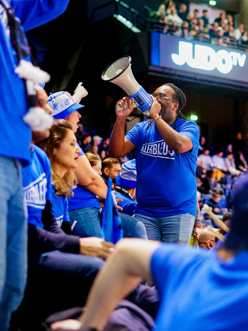 Leader d'ambiance faisant vibrer nos athlètes et les tribunes à l'aide d'un mégaphone.